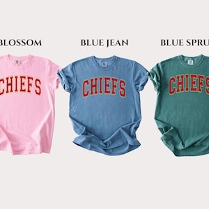 Op de afbeelding: Drie T-shirts met korte mouwen en ronde hals in lichtroze, middenblauw en donkergroenblauw. Elk shirt heeft het woord CHIEFS in een rood gebogen lettertype met een gele omlijning op de borst. De kleuren zijn Blossom, Blue Jean en Blue Spruce.