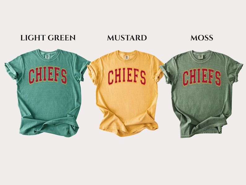 Op de afbeelding: Drie T-shirts met korte mouwen en ronde hals in de kleuren lichtgroen, mosterdgeel en mosgroen. Elk shirt heeft het woord CHIEFS in een rood gebogen lettertype met een gouden omlijning op de borst. De labels LIGHT GREEN, MUSTARD, MOSS staan erboven.