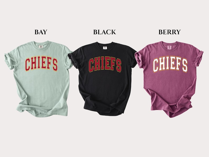 Op de afbeelding: Drie t-shirts met korte mouwen in de kleuren bay, zwart en berry. Elk shirt heeft het woord CHIEFS in een gebogen, collegiale lettertype op de borst gedrukt. Het bay shirt heeft rode tekst, het zwarte shirt heeft rode tekst en het berry shirt heeft witte tekst.