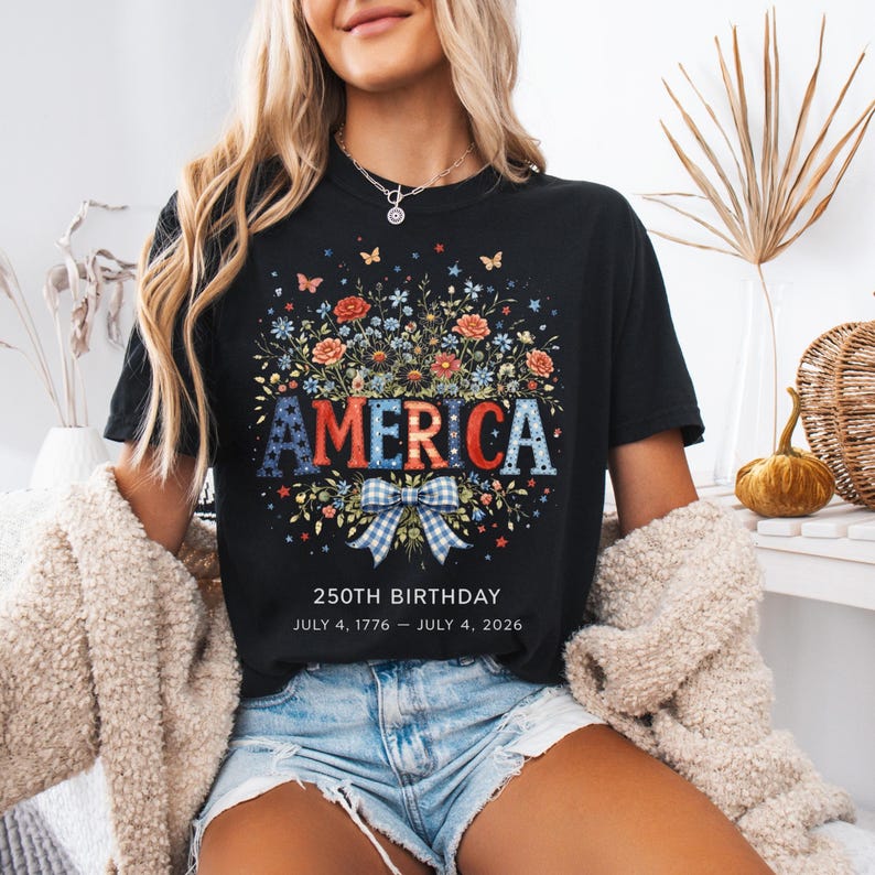 May include: Black t-shirt with a floral design and the word "AMERICA" in red, white, and blue. The shirt also features the text "250TH BIRTHDAY JULY 4, 1776 &ndash; JULY 4, 2026".