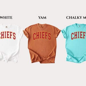 Op de afbeelding: Drie T-shirts met korte mouwen en ronde hals in de kleuren wit, yam en chalky mint. Elk shirt heeft het woord CHIEFS in een rood gebogen lettertype met een gele omlijning op de borst. De labels WHITE, YAM en CHALKY MINT staan erboven afgebeeld.