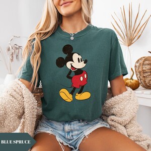 May include: Blue spruce t-shirt featuring a vintage-style Mickey Mouse graphic. The cartoon character is depicted in black, red, yellow, and white. The shirt has short sleeves and a crew neck. The text "BLUE SPRUCE" is at the bottom of the image.