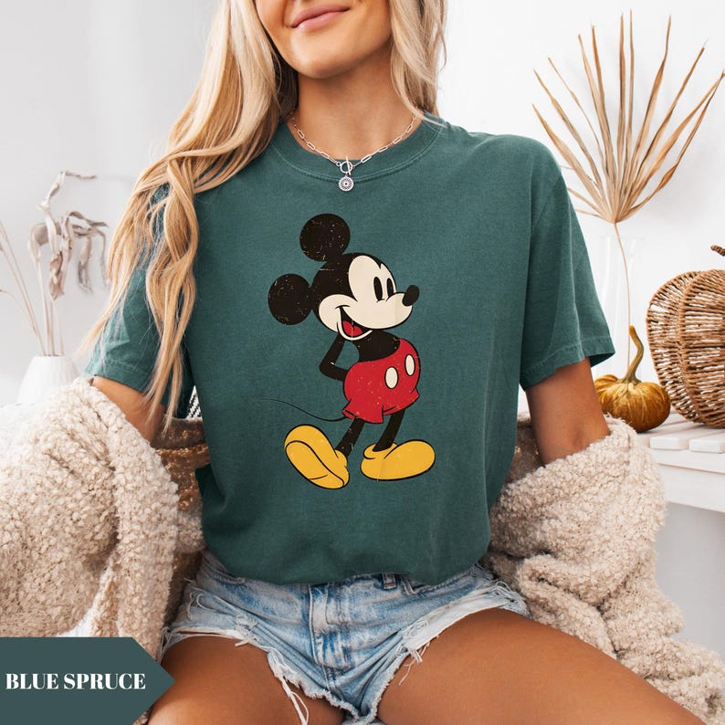 May include: Blue spruce t-shirt featuring a vintage-style Mickey Mouse graphic. The cartoon character is depicted in black, red, yellow, and white. The shirt has short sleeves and a crew neck. The text "BLUE SPRUCE" is at the bottom of the image.