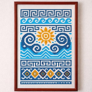 Op de afbeelding: Ingelijst kruissteekkunstwerk met een geometrisch ontwerp in blauw, wit en geel. Het ontwerp bevat golfpatronen, een zon en andere geometrische vormen. Het kunstwerk is ingelijst in een bruine houten lijst.