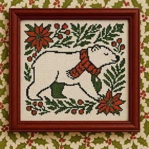 May include: Cross-stitch artwork of a polar bear wearing a red scarf, surrounded by green foliage and red poinsettias. The artwork is framed in a dark brown wooden frame, perfect for holiday decor.