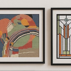 May include: Two framed cross-stitch artworks. One features an abstract design with orange, green, and blue hues. The other is a vertical geometric pattern with orange, green, and white elements, resembling stained glass. Both are in black frames.
