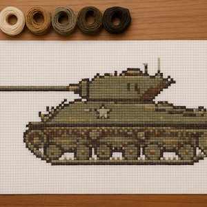 May include: A cross-stitch pattern of a military tank in shades of green and brown, with a white star on the side. The tank is on a white grid fabric, with spools of thread in various earth tones above.