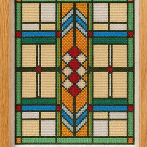 Könnte beinhalten: Ein gerahmtes Kreuzstich-Kunstwerk mit einem geometrischen Design im Stil von Buntglas. Das Design enthält Quadrate, Rechtecke und Rauten in Gelb-, Grün-, Blau-, Rot- und Weißtönen, vor einem dunkelgrünen Hintergrund. Der Rahmen besteht aus hellbraunem Holz.