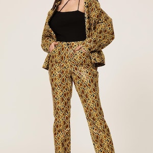 Może przedstawiać: Kobieta w garniturze ze wzorem wężowej skóry i czarnym topie. Garnitur ma brązowo-złoty wzór. Marynarka jest otwarta, a spodnie proste. Kobieta ma również na sobie czarne szpilki.