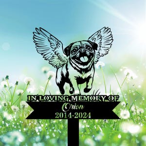 May include: A black metal garden stake featuring a pug with angel wings, with the text "IN LOVING MEMORY OF Orion 2014-2024". The pug is smiling with its tongue out, set against a background of grass and dandelions.