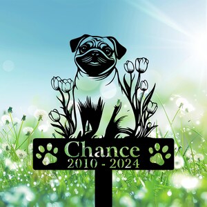 May include: Black metal garden stake featuring a pug dog design with floral accents. The stake includes the name "Chance" and the years "2010-2024". The design is set against a backdrop of grass and a blue sky.