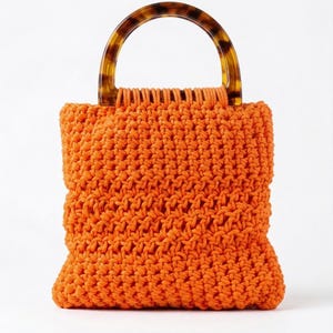 Puede incluir: Bolso tote naranja tejido a mano con un asa de carey. El bolso está hecho de hilo grueso y texturizado y tiene una forma redondeada. El asa tiene forma curva y semicircular.
