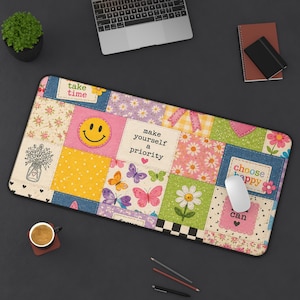 以下が含まれることがあります： パッチワークデザインの長方形マウスパッド。スマイリーフェイス、蝶、花、そして「take time」、「make yourself a priority」、「choose happy」というフレーズが特徴です。パッドは、ラップトップなどがある暗い表面にあります。