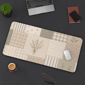 Op de afbeelding: Een rechthoekige bureaumat met een patchwork ontwerp in beige, crème en groen. De mat heeft geborduurde bloemendetails en een centraal boeket. Een witte computermuis ligt op de mat.