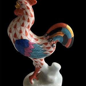 May include: A porcelain rooster figurine with a red, white, blue, and gold painted design. The rooster is standing on a white base.