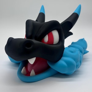 Puede incluir: Una escultura de cabeza de dragón impresa en 3D en negro y azul. El dragón tiene ojos rojos y blancos, dientes blancos y una boca rosa. Los cuernos son negros con puntas azules. La escultura está sobre un fondo blanco.