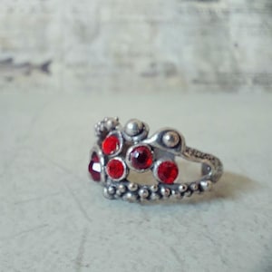 Könnte beinhalten: Ein silberner Ring mit einem Kronendesign, das mit roten Edelsteinen besetzt ist.