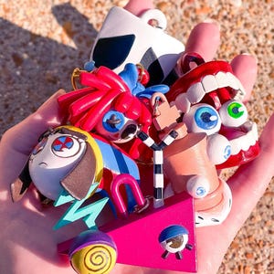May include: A collection of colorful, whimsical art pieces, including a pink geometric shape, a cartoon face, and a pair of red lips. The pieces are painted with bright colors and bold lines, creating a playful and unique aesthetic.