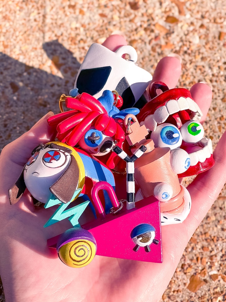 May include: A collection of colorful, whimsical art pieces, including a pink geometric shape, a cartoon face, and a pair of red lips. The pieces are painted with bright colors and bold lines, creating a playful and unique aesthetic.