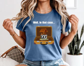 Peut inclure: T-shirt bleu avec l'inscription "Well, in that case..." au-dessus d'une illustration de puits de dessin animé dans une valise. Le puits a un toit en bois et un visage souriant.