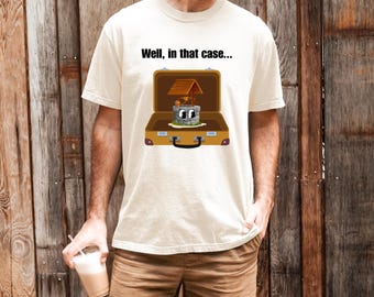 Peut inclure: T-shirt crème avec un dessin d'un puits de dessin animé dans une valise, avec le texte "Well, in that case...". Le puits a un toit en bois et un visage souriant. La valise est marron avec une poignée noire.