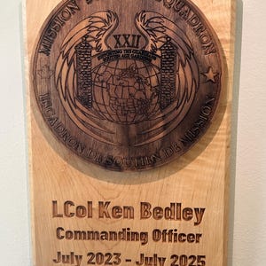 May include: Wooden plaque with a circular emblem and text. The emblem features wings, a globe, and the text "MISSION SUPPORT SQUADRON." Below, the plaque reads "LCol Ken Bedley, Commanding Officer, July 2023 - July 2025."