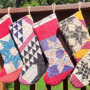 Könnte beinhalten: Vier handgefertigte Weihnachtsstrümpfe mit gesteppten Patchwork-Designs. Jeder Strumpf hat ein anderes Muster, darunter Sterne und geometrische Formen, in einer Vielzahl von Farben wie Rot, Blau, Schwarz und Gelb. Sie hängen an einem Holzgeländer.