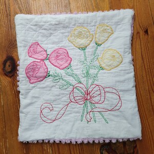 May include: A white pillow with a pink and yellow embroidered floral design. The pillow has a pink crocheted trim around the edges.