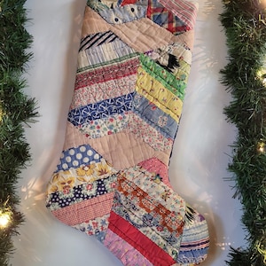 May include: A Christmas stocking constructed from a patchwork of various vintage fabric scraps in diverse colors and patterns, including floral, plaid, polka dot, and anchor prints, featuring visible quilted stitching and a small jute hanging loop.