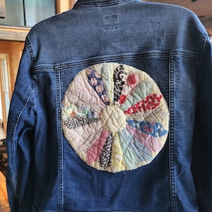 May include: A blue denim jacket with a colorful patchwork quilt design on the back. The quilt is a circular design with a variety of colors and patterns.