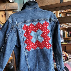 May include: A blue denim jacket with a red and white patchwork quilt design on the back.