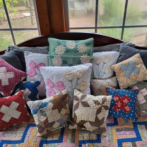 May include: A collection of vintage patchwork cushions in various colours and patterns, including red, blue, green, and white. The cushions are arranged on a bed with a patchwork quilt.