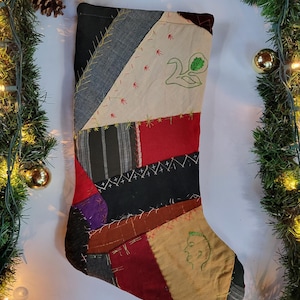 May include: A patchwork Christmas stocking in various fabrics and colours, including red, black, and tan. The stocking has embroidered details, such as a swan and a profile. A jute loop is attached for hanging.