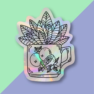 May include: A holographic sticker of a mug with a leafy plant growing out of it. The mug is filled with oranges and orange slices.