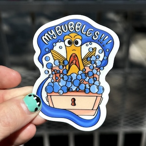 Può includere: Un pesce giallo dei cartoni animati con occhi grandi e una bocca aperta è intrappolato in un forziere blu pieno di bolle blu. Il forziere ha un buco della serratura ed è circondato da un'onda blu. Il testo "My Bubbles!!" è scritto in un vortice blu e bianco sopra il forziere.