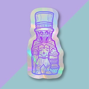 May include: A holographic sticker featuring a purple and blue illustration of a skeletal figure wearing a top hat and holding a container. The figure is standing on a platform with a geometric pattern.