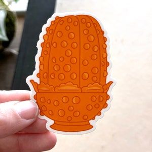 May include: Orange ceramic planter with a textured, bubble-like design. The planter has a wide, round base and a scalloped rim.