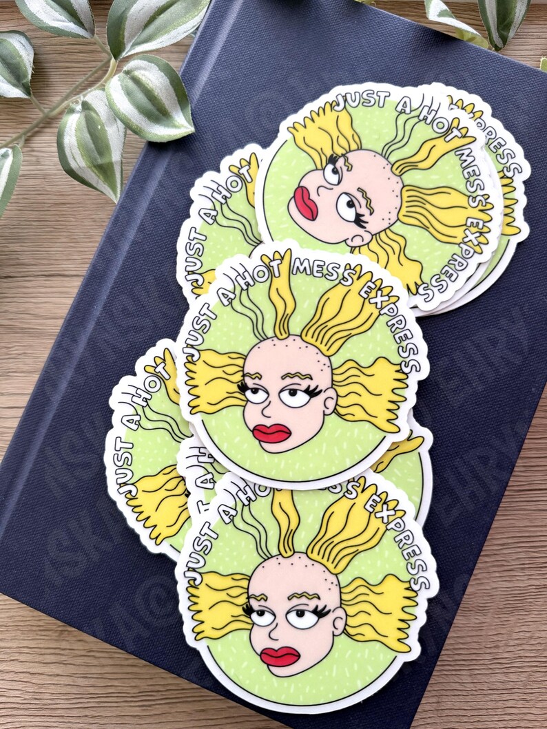 May include: A stack of round stickers featuring a cartoon character with yellow hair and red lips. The stickers have a light green background and the text "JUST A HOT MESS EXPRESS" in a circular pattern.