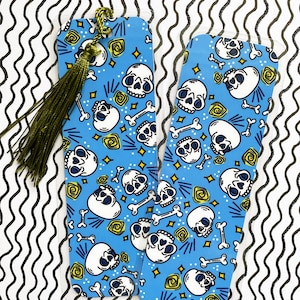 May include: Two blue and white skull bookmark with a gold tassel. The bookmarks have a repeating pattern of skulls, bones, and swirls.