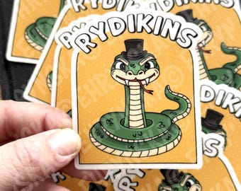 May include: A collection of stickers featuring a cartoon snake wearing a top hat. The snake is green with a white belly and a red tongue. The stickers have the word "RYDIKINS" in a circular design around the snake.