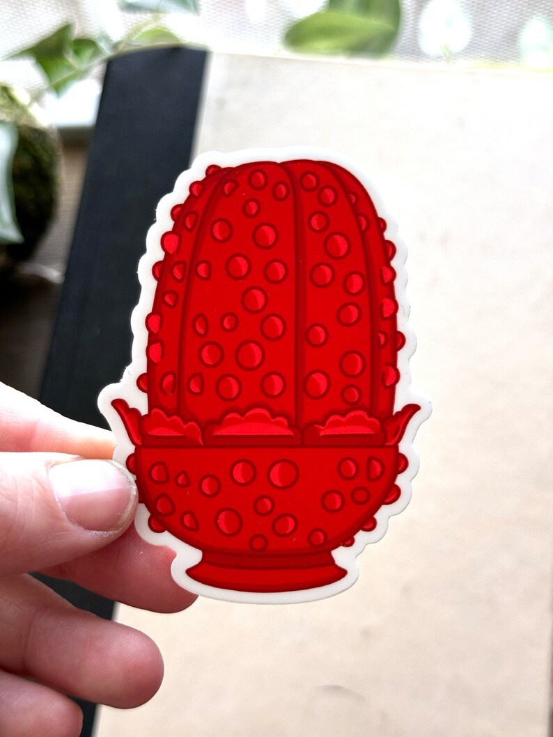 May include: A red, cartoon-style, ceramic planter with a textured, dotted surface. The planter has a wide, round base and a narrow, cylindrical top.