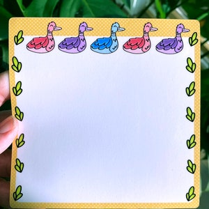 May include: A yellow notepad with a white background and a border of green leaves and pink, purple, and blue ducks.