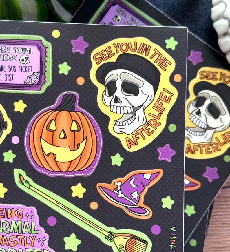 Peut inclure: Planches d'autocollants noirs avec des illustrations sur le th&egrave;me d'Halloween. Les motifs comprennent une citrouille souriante, un cr&acirc;ne portant un chapeau avec le texte "SEE YOU IN THE AFTERLIFE!", un chapeau de sorci&egrave;re et un balai. Les autocollants sont entour&eacute;s d'&eacute;toiles et de points.