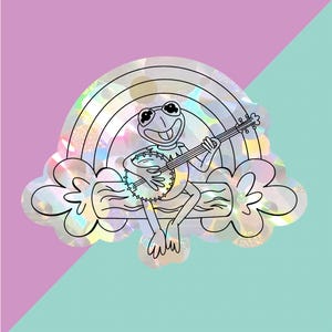 Puede incluir: Una pegatina caprichosa con una rana de dibujos animados tocando el banjo. La rana está sentada en un tronco frente a un arcoíris y nubes. El diseño tiene un acabado holográfico iridiscente, sobre un fondo rosa y turquesa.