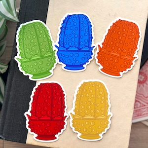May include: Five colorful glass dish stickers. The stickers are shaped like a small bowl with a rounded top. The stickers are green, blue, orange, red, and yellow.