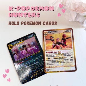 May include: Two holographic Pokemon cards with the text "K-Pop Demon Hunters" and "Holo Pokemon Cards." One card features "Saja Boys" and the other "HUNTRIX." The cards have colorful graphics and text.