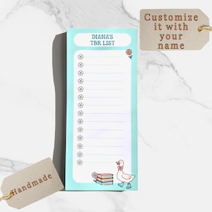 May include: A light blue TBR (To Be Read) list notepad with the text "DIANA'S TBR LIST". The notepad features a daisy border, a stack of books, and a cartoon duck wearing boots. A brown tag says "Customize it with your name".