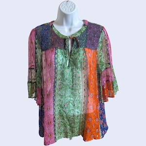 May include: A multi-colored blouse featuring a patchwork design with vertical panels of pink, green, orange, and blue. The garment has three-quarter length bell sleeves, a round neckline with a tie closure, and a textured, semi-sheer fabric.