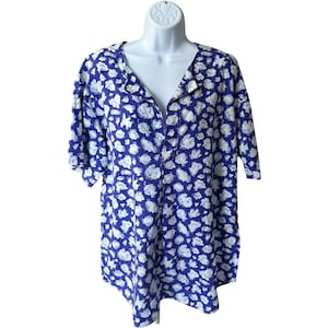 May include: A blue button-down shirt with a white cloud pattern. The short-sleeved shirt has a V-neck and is displayed on a white mannequin. The cloud pattern is repeated across the entire shirt.