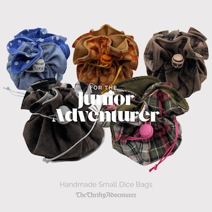 May include: Five handmade small dice bags in various patterns and colors. The bags include blue polka dots, orange and brown floral, brown tweed, dark brown, and red and green plaid. Text reads "For the Junior Adventurer" and "The Thrifty Adventurer".